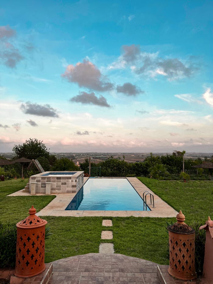 Luxury swimming pool with lush garden view and expansive sky, perfect for relaxation.